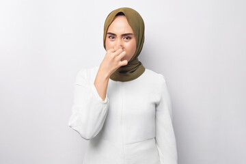 unhappy young beautiful Asian Muslim woman 20s wearing hijab feeling disgusted, holding her nose to avoid smelling foul, looking camera isolated on white background. People religious lifestyle concept