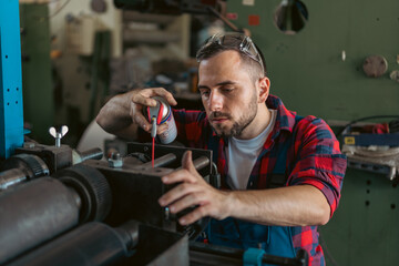 A young Caucasian worker in the workshop lubricates the gears on the machine with lubricating spray