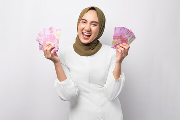 Excited beautiful young Asian Muslim woman wearing hijab holding cash money in rupiah banknotes...