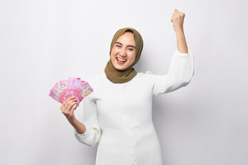 Excited beautiful young Asian Muslim woman wearing hijab holding cash money in rupiah banknote and...