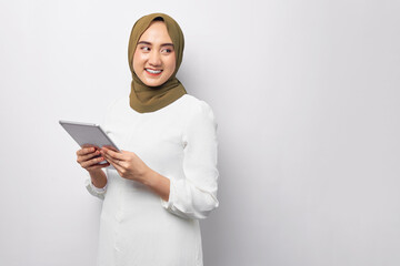 Beautiful smiling friendly young Arabian Asian Muslim woman wearing hijab green holding digital tablet while looking at empty space isolated on white background. People religious lifestyle concept