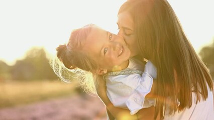 family day. young mom and little daughter enjoy relaxing in a field with lavender at sunset. A beautiful mother hugs and kiss child girl tightly. Maternal care and love for the child. mothers day. - Powered by Adobe