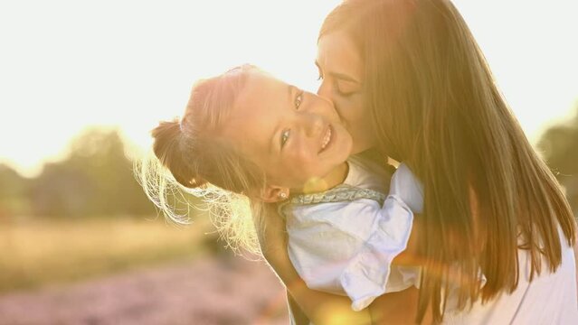 family day. young mom and little daughter enjoy relaxing in a field with lavender at sunset. A beautiful mother hugs and kiss child girl tightly. Maternal care and love for the child. mothers day.