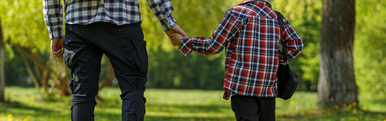 Rear on Caucasian father and little son with backpack walking the park or forest on summer day.