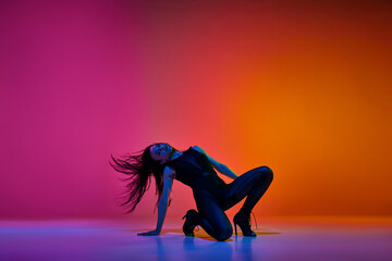 Passion in movements. Young woman performing high heel stiletto dance over gradient pink red studio...