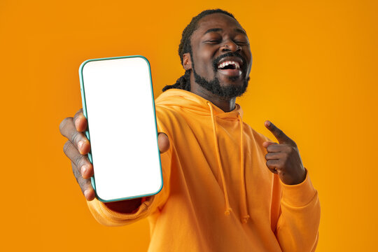 Smiling african man pointing at cellphone with blank screen with copy space