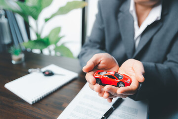 Business woman's hand protecting red toy car on desk. Planning to manage transportation finance costs. Concept of car insurance business, saving buy - sale with tax and loan for new car. - obrazy, fototapety, plakaty