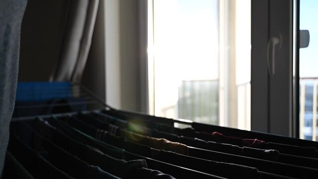 Person taking clothes off expandable drying rack standing near window
