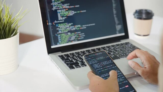 Software developer hands typing data coding programming javascript with laptop computer and mobile phone, Programmer woman looking smartphone program code at workplace, IT startup concept