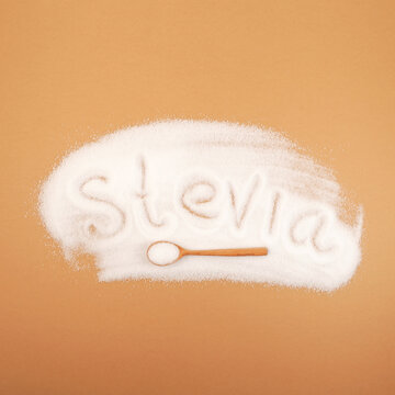 Sugar substitute in wooden scoop on beige background. Scattered stevia sweetener with an inscription Stevia. Stevioside powder or Stevia sweetener. Natural Extract. Food additive E960