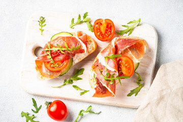 Open sandwiches with prosciutto and arugula on cutting board at white background. Top view.