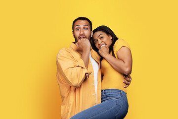 Fototapeta premium Frightened excited young african american couple, lady biting fists, afraid, isolated on yellow background, studio