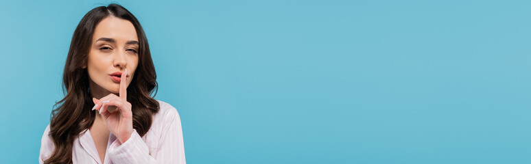 brunette young woman in sleepwear showing hush sign isolated on blue, banner.