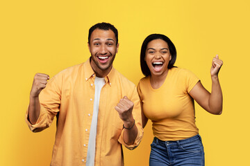 Glad excited young african american couple shouting, have fun, make success sign with hand in free time