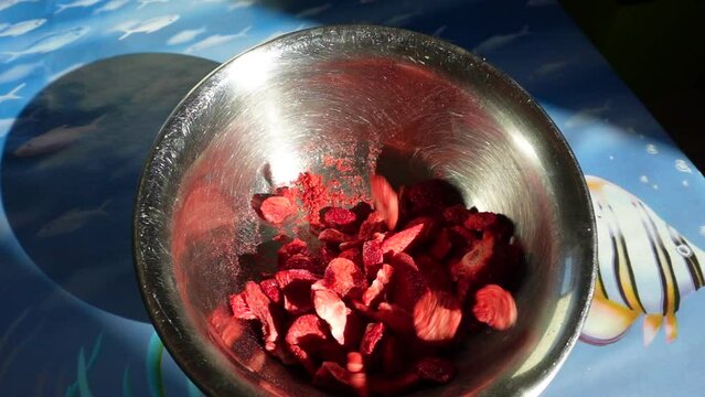 Some strawberry chips are falling down into the snack bowl . Chips snack in a silver bowl ready to eat . Healthy , red but beautiful yummy food . Flying strawberry flips puffs concept footage .