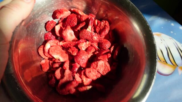 Some strawberry chips are swayed inside the snack bowl . Chips snack in a silver bowl ready to eat . Healthy , red but beautiful yummy food . Flying swayed strawberry flips puffs concept footage .