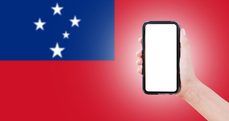 Close-up of male hand holding smartphone with blank on screen, on background of blurred flag of Samoa.