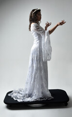 Fototapeta na wymiar Full length portrait of beautiful woman wearing fantasy costume, white bridal gown. standing pose, gestural arm movements casting a spell. Isolated white studio background. 