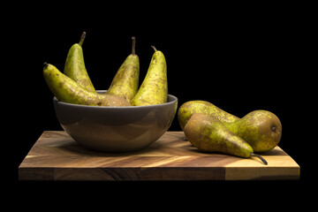 Pears in a bowl and on a wooden cutting board, isolated on black