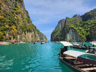 Many tourist boats in the blue lagoon among the mountains of Maya Bai island.