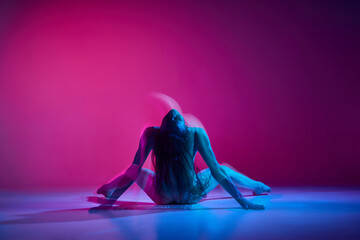 Passionate movements. Young woman dancing in bodysuit over gradient pink studio background in neon with mixed lights. Concept of contemporary dance style, art, aesthetics, hobby, creative lifestyle