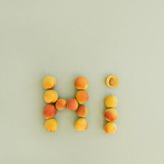 Fototapeta na wymiar Word Hi made of ripe fruits peaches on bright green background. Flat lay, top view
