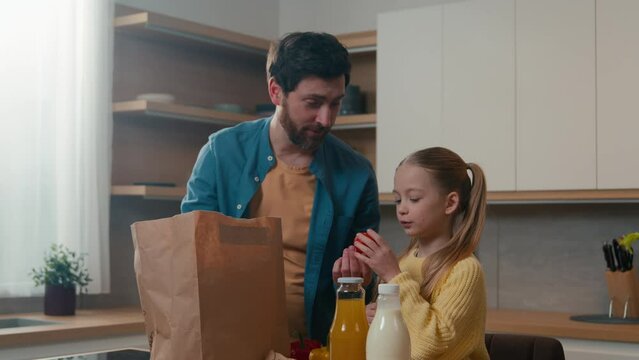 Caucasian family adult father dad with kid child girl little daughter standing in kitchen unpack paper shopping bag with food vegetables get out fresh natural products e-store delivery services online