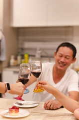 Asian man having a celebration with friends toasting glass of red at dinner party.