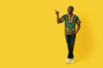Fototapeta na wymiar Cheerful black man in traditional shirt pointing at copy space