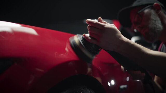 Red Sportscar Standing in a Stylish Detailing Dealership Studio. Professional Worker Buffing the Body from Light Scratches, Removing Swirls and Paint Defects from a Fender of the Vehicle