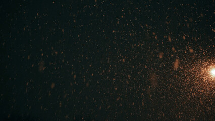 Obraz premium Snowflakes fall from the sky on the background of a residential building with burning lights in the windows at night.