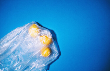 Lemon fruits in transparent plastic bag on blue background. Concept about plastic pollution, microplastics in environment, problems in ecosystems. Minimal style, flat lay, top view, copy space.