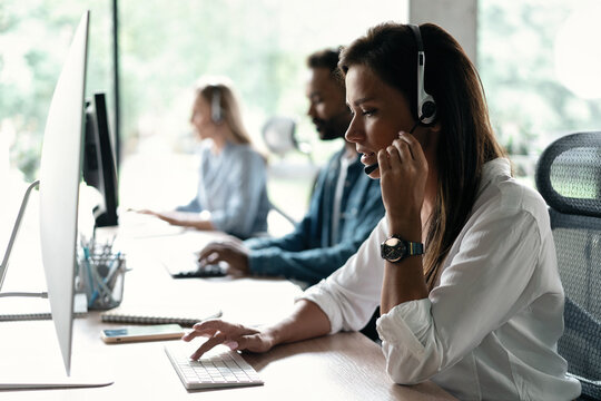 Friendly smiling woman call center operator with headset using computer at office.
