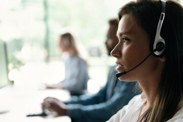 Friendly smiling woman call center operator with headset using computer at office.