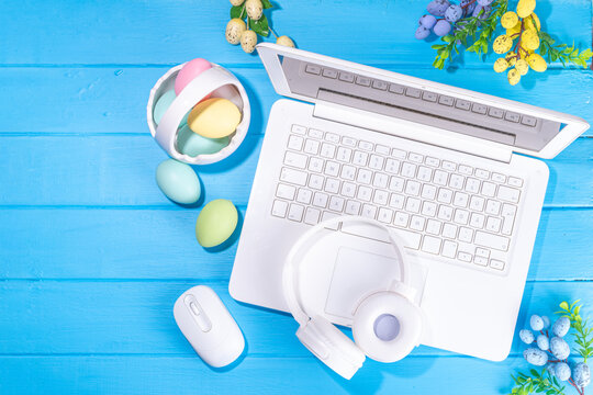 Easter office workplace, preparation for holiday, spring Easter sale, blogging. White laptop keyboard with easter eggs basket and flower branch decorations, on light blue wooden table top view 