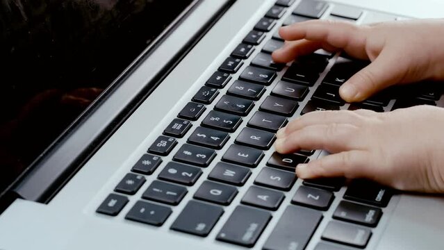 Todler hands trying ti type on laptop keyboard, playing games since childhood. Problem with new technology and growing of a child.