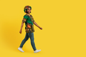 Fototapeta na wymiar Cheerful black woman in traditional outwear walking towards copy space