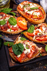 Hot loaded pizza sandwiches with tomatoes, mozzarella cheese and pepperoni, on dark background with herbs, olive oil and spices