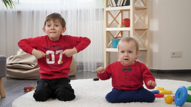 Funny shot of little baby boy with plder brother dancing and being silly on carpet on living room. Concept of child education, baby development, family having fun and playing games.