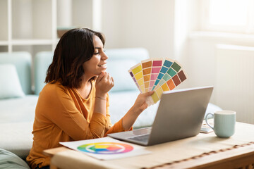 Middle Eastern Female Freelancer Holding Color Swatches And Using Laptop At Home