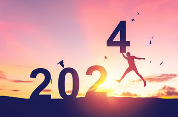 Man jumping on sunset sky with birds flying at top of mountain and number 2024 abstract background. Happy new year and holiday concept.