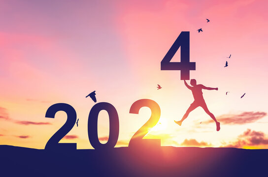 Man jumping on sunset sky with birds flying at top of mountain and number 2024 abstract background. Happy new year and holiday concept.