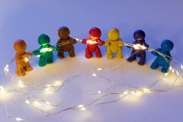 Figuren aus Knete halten eine Lichterkette, symbolische Darstellung für Zusammenhalt. 