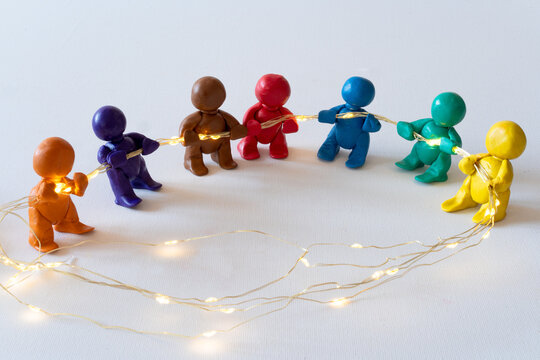 Figuren aus Knete halten eine Lichterkette, symbolische Darstellung für Zusammenhalt. 