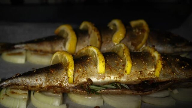 Two whole appetizing fish with lemon on onion rings on parchment in the oven close-up. The process of cooking baked fish in the oven.