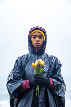 Woman in raincoat holding yellow tulips near sea