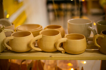Clay cups stand on a wooden rack, shelf.