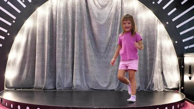 A cute little girl is dancing on the children's stage in the playroom.