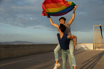 Happy young couple with rainbow flag. Two men enjoy outside.
