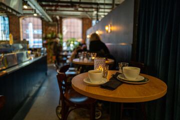 Indoor restaurant setup with empty coffee mugs and glasses on the wooden table with people sitting in the background
